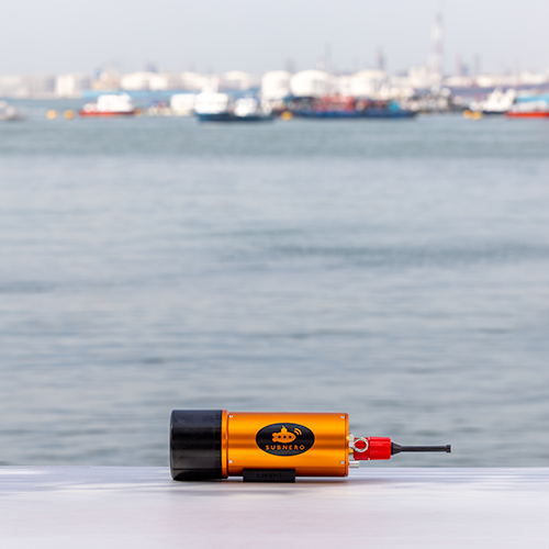 Subnero L12L Series Silver Edition acoustic smart modem on a dockside ledge with a harbor in the background, ready for long-range underwater deployment